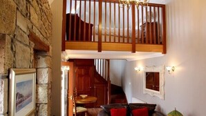 A cozy interior with a stone wall, a wooden staircase, a dining area, and a living room with a leather sofa. - Auchenheglish Lodges - The Smiddy (Alexandria)