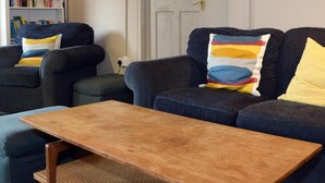 A living room with two dark sofas, a wooden coffee table, and a bookshelf filled with books. - Gallt y Glyn (Caernarfon)