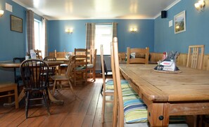 A dining area with wooden tables and chairs, a buffet table with food and condiments, and a view of the outdoors through a window. - Gallt y Glyn (Caernarfon)
