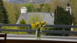 A view from a balcony with a mountain backdrop, a white building with a chimney, and a bench with a vase of flowers. - Gallt y Glyn (Caernarfon)