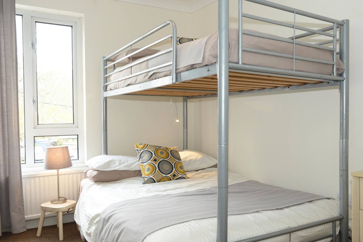 A bunk bed with a window, a bedside table, and a lamp.