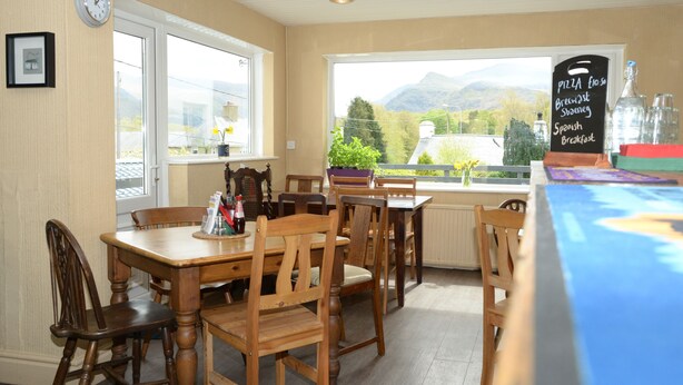 A restaurant with wooden tables and chairs, a view of mountains through the window, and a chalkboard menu. - Gallt y Glyn (Caernarfon)