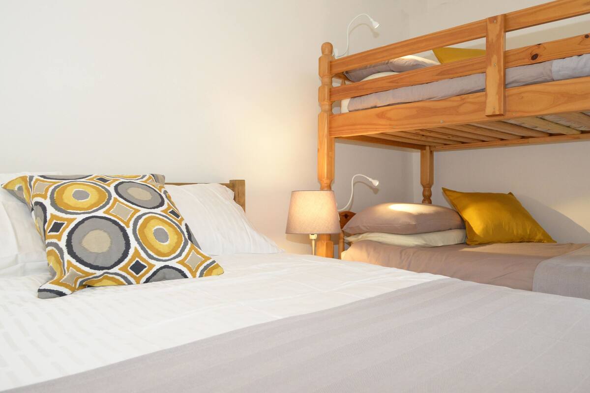 A bunk bed with a wooden frame, a bedside table with a lamp, and patterned pillows.