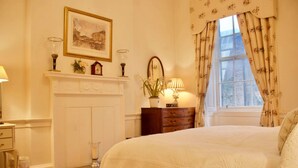 A bedroom with a large bed, a fireplace, a dresser, and a window with curtains.