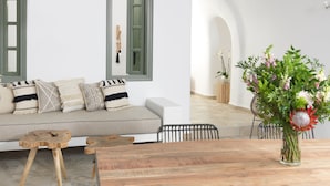 A modern living room with a wooden dining table, a sofa with patterned cushions, and a large window with a view of the outdoors. - Drops Cave Houses (Santorini)