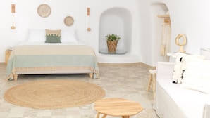 A bedroom with a bed, bedside table, and a small round table. - Drops Cave Houses (Santorini)