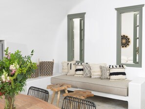 Ein modernes Wohnzimmer mit einem weißen Sofa, Fenstern mit grünem Rahmen und verschiedenen gemusterten Kissen.