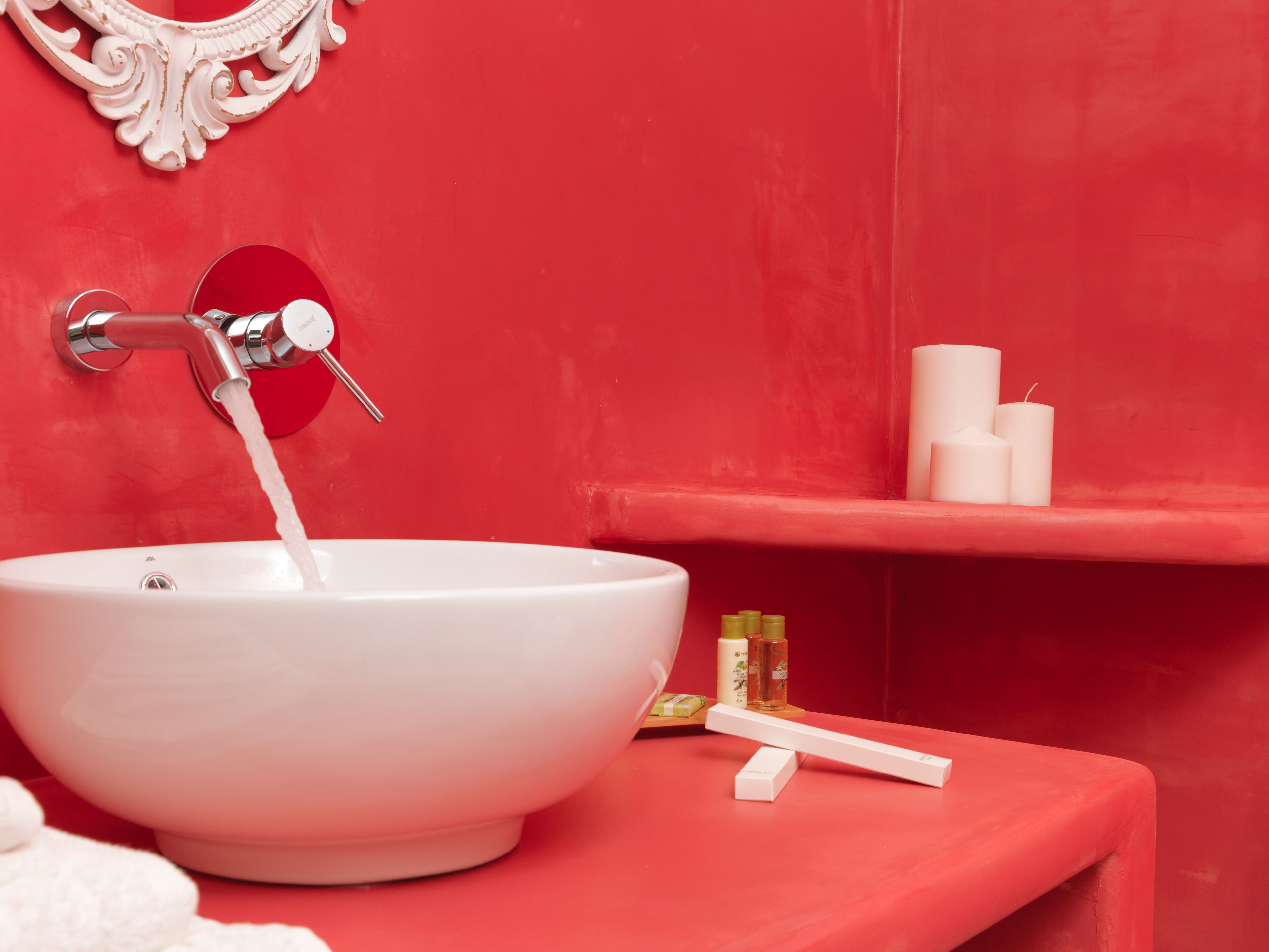 Un baño con un lavamanos blanco, una pared roja y un estante con artículos de aseo.