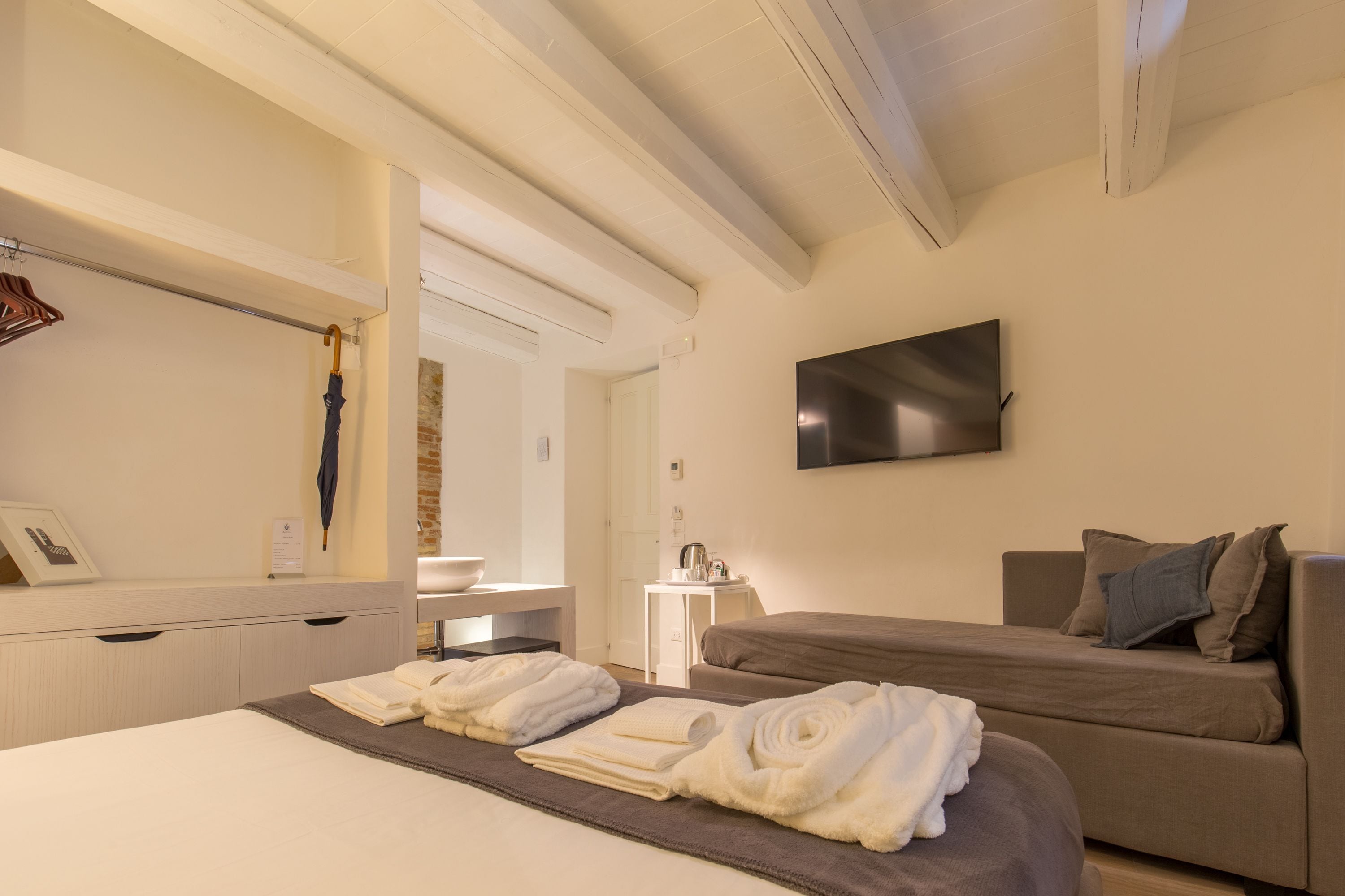 A hotel room with a bed, a sofa, a flat-screen TV, and a small table with a kettle.