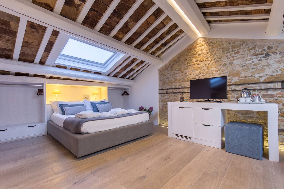 Ein Schlafzimmer mit Bett, Fernseher, Steinwand und Oberlicht.