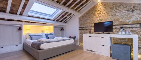 Un dormitorio con cama, televisor, pared de piedra y tragaluz.