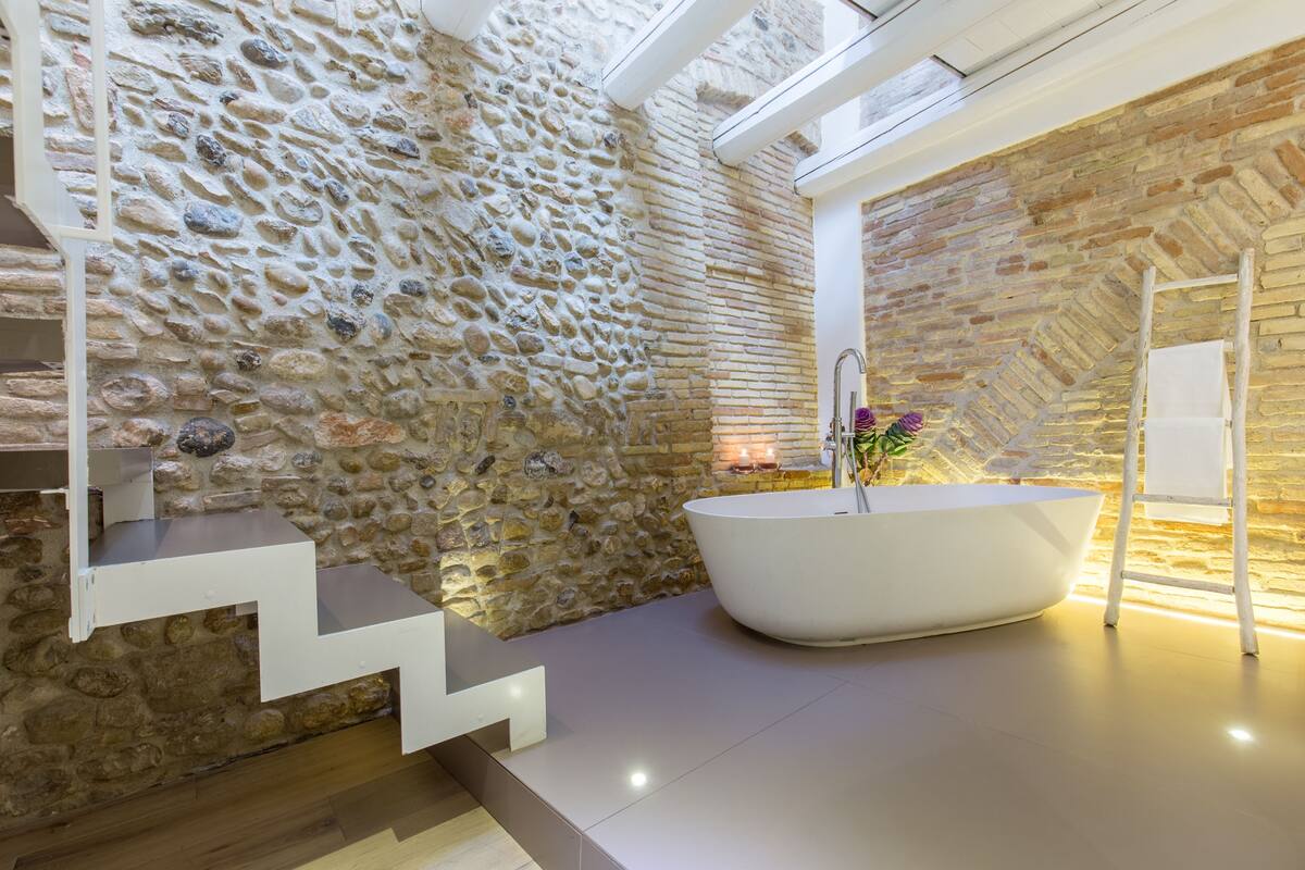 Ein modernes Badezimmer mit Steinwand, freistehender Badewanne und einer Treppe.