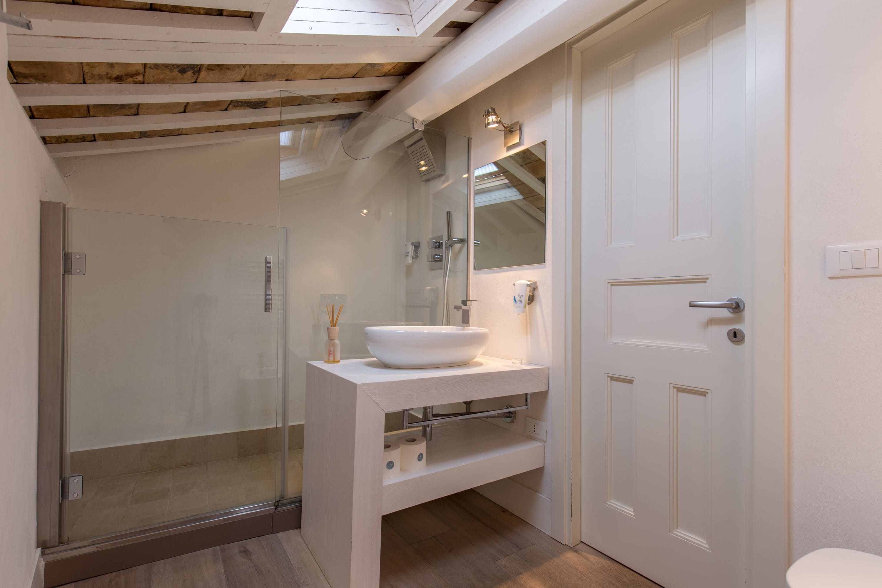 Ein modernes Badezimmer mit einer gläsernen Duschkabine, einem weißen Waschbecken und einer Tür mit Griff.