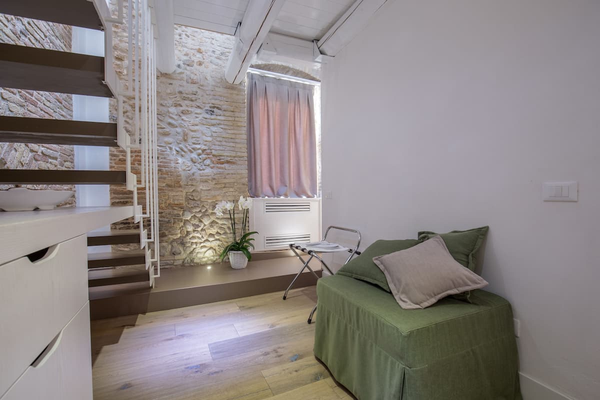 Ein Schlafzimmer mit einem grünen Bett, einem weißen Stuhl, einer Topfpflanze und einer Treppe, die zu einer Steinwand führt.