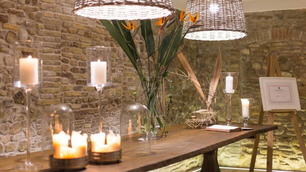 Une table en bois avec des bougies, un vase avec des plantes et un certificat posé sur un présentoir.