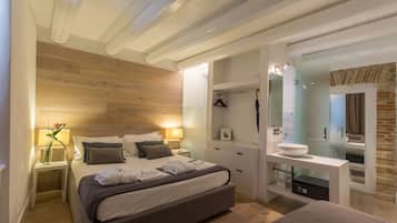 Un dormitorio moderno con techo de madera, una cama con toallas ordenadas, una mesita de noche con lámpara y un baño con espejo y lavabo.