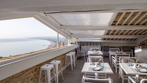 Une terrasse avec des meubles blancs, un mur en pierre et une vue sur la mer.