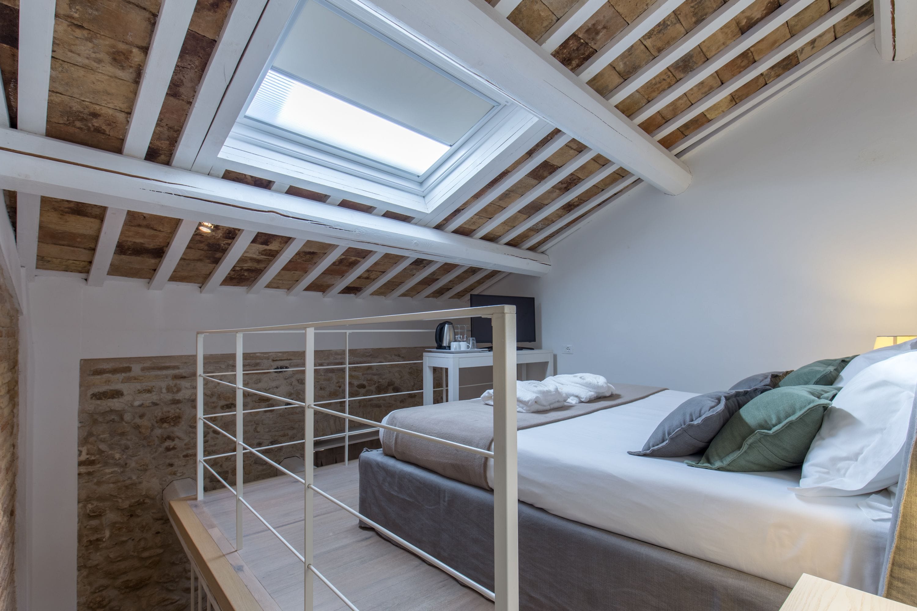 A loft-style bedroom with a skylight, a bunk bed, and a bedside table with a lamp.