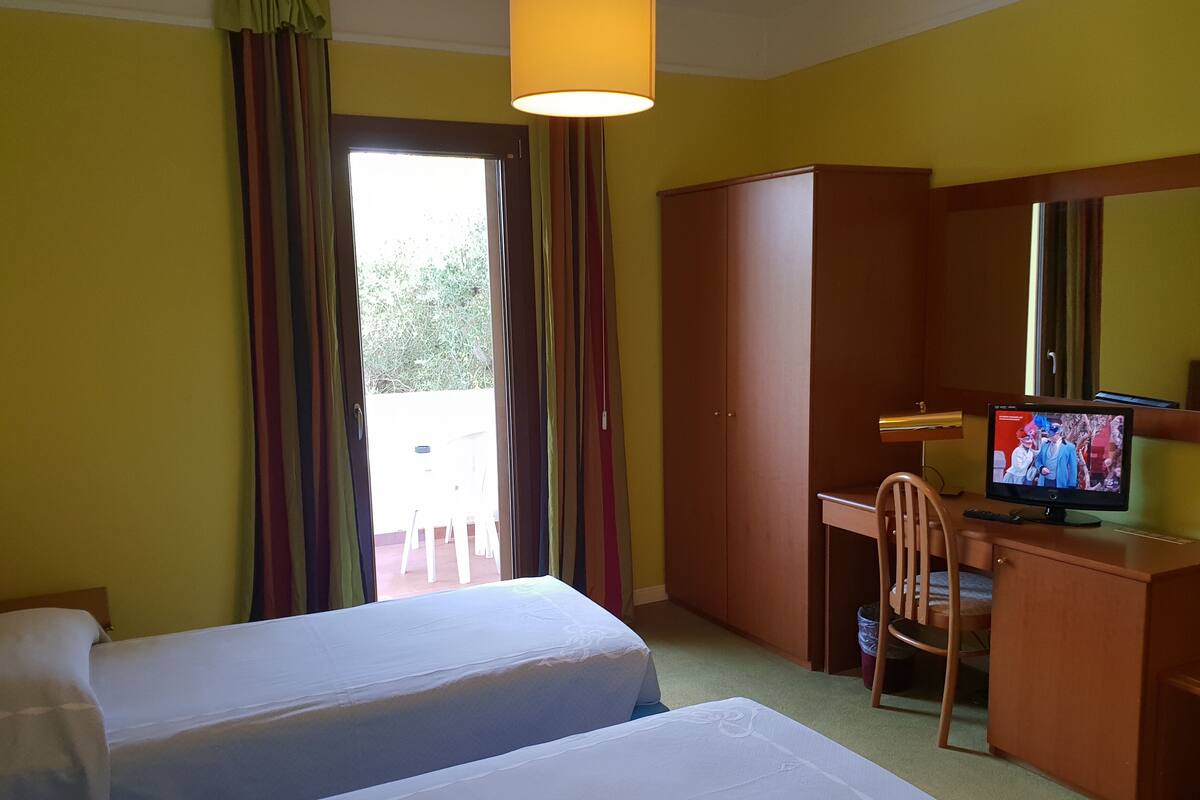 A hotel room with two beds, a desk with a television, and a wardrobe.