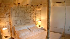 Un dormitorio rústico con pared de ladrillo, cama con dosel, lámpara de noche y una pequeña mesa redonda.