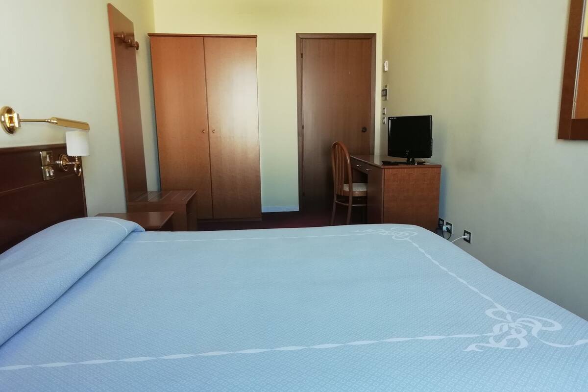 A hotel room with a bed, a desk, a chair, a television, and a wardrobe.