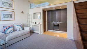 Eine moderne Wohnung mit Schlafgalerie, einer Küchenzeile und einem Wohnbereich inklusive Sofa und gerahmten Bildern.