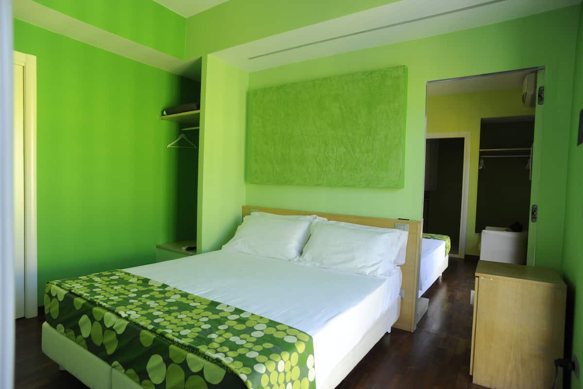 Um quarto com cama, guarda-roupa, mesa de cabeceira e parede verde.