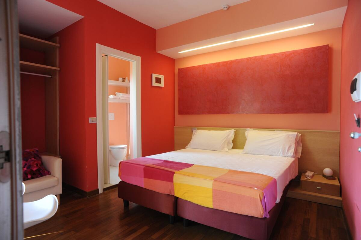 Quarto de hotel com cama, mesa de cabeceira, cadeira, armário e banheiro.