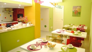 A brightly colored dining area with tables set for meals, a kitchen in the background, and a door leading to another room.
