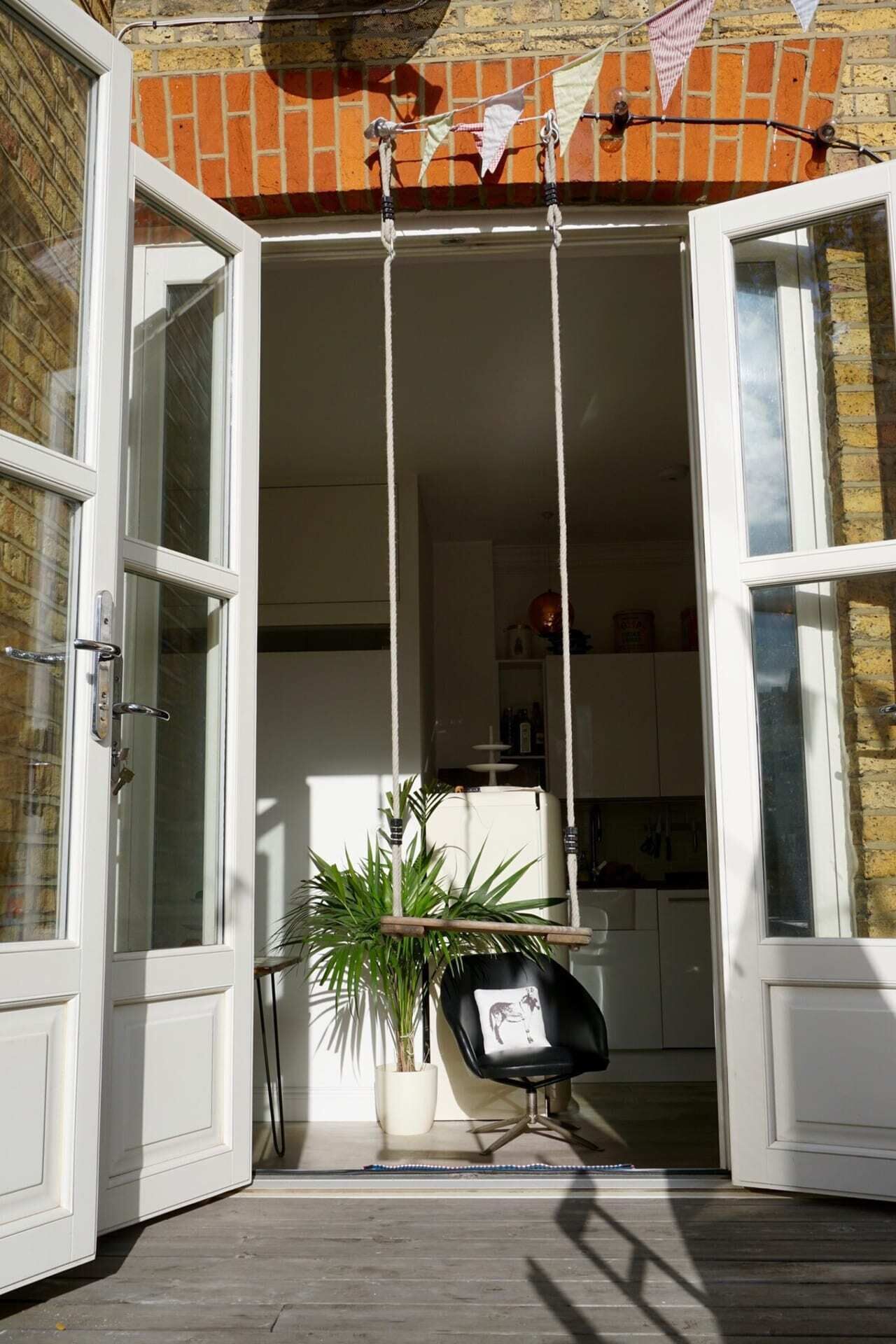 An open door leading to a kitchen with a potted plant and a black chair.