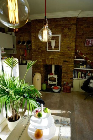 A cozy living room with a brick fireplace, a white stove, and a bookshelf filled with books. - Beautiful Canalside 1-bedroom Flat With Terrace (London)