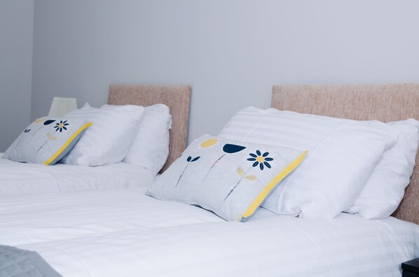 Cama bem arrumada com roupa de cama branca e travesseiros decorativos com estampas florais.