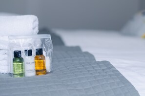 A neatly made bed with a grey quilt, a white towel, and three toiletry bottles on the side. - Elforma - Barony Suite (Edinburgh)