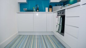 A kitchen with white cabinets, a blue backsplash, and a striped floor. - Elforma - Barony Suite (Edinburgh)