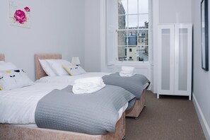 Quarto de hotel com duas camas, janela com vista para a cidade, guarda-roupa e uma pintura floral na parede.