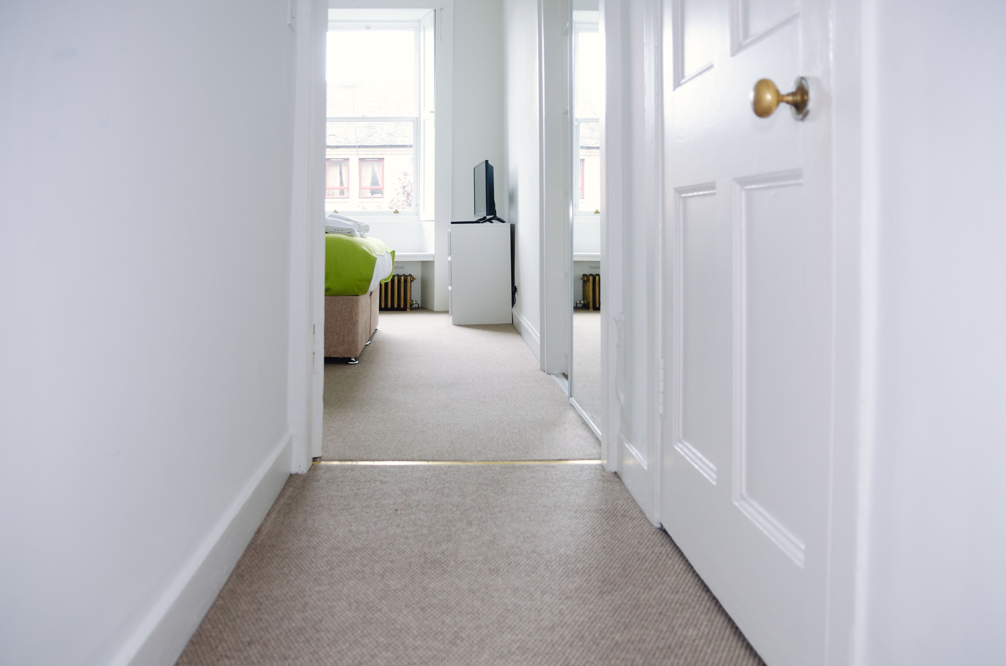 A hallway leading to a bedroom with a bed, a television, and a radiator.