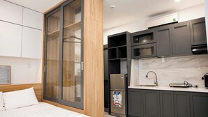 A modern hotel room with a bed, a sliding glass door closet, a kitchenette with a sink, and a refrigerator. - The Sargon (Ho Chi Minh City)