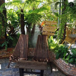 Two wooden lounge chairs with a brick wall and lush greenery in the background. - Sena Botanic (Ho Chi Minh City)