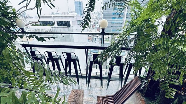 An indoor terrace with chairs and tables, surrounded by lush greenery and a city view. - The Sargon (Ho Chi Minh City)