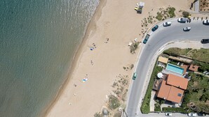 Vista aérea de uma praia com uma estrada serpenteando ao redor, uma piscina e vários carros estacionados.