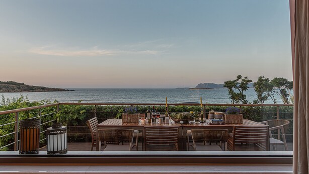 Varanda com vista para o mar, mobiliário de madeira e mesa posta para refeições.