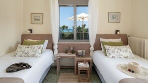 Quarto com duas camas, uma mesinha e vista para o mar pela janela.