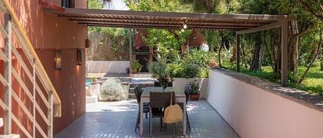 Une terrasse extérieure avec une table et des chaises, entourée de plantes en pot et d’une pergola.