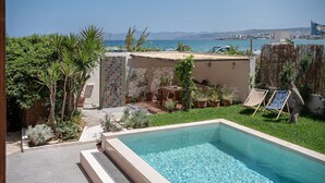 Piscina com vista para o mar, rodeada por vegetação e um pequeno alpendre.