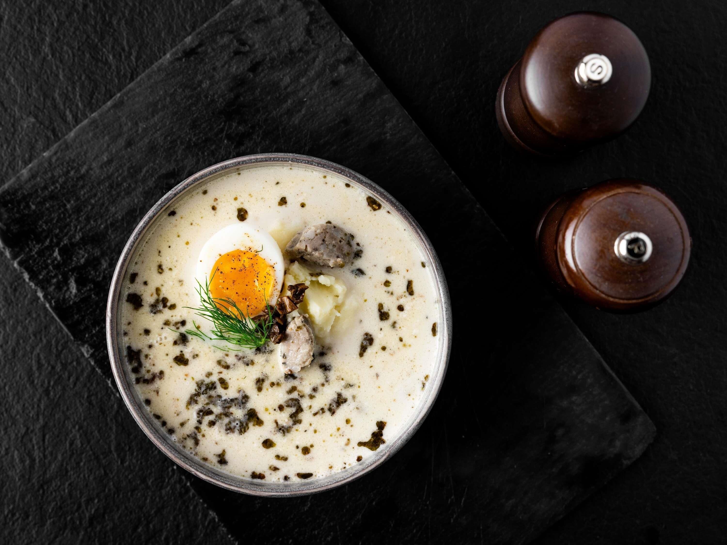 Un bol de soupe crémeuse, garni d’un œuf poché, de viande et d’herbes, servi sur une ardoise sombre.