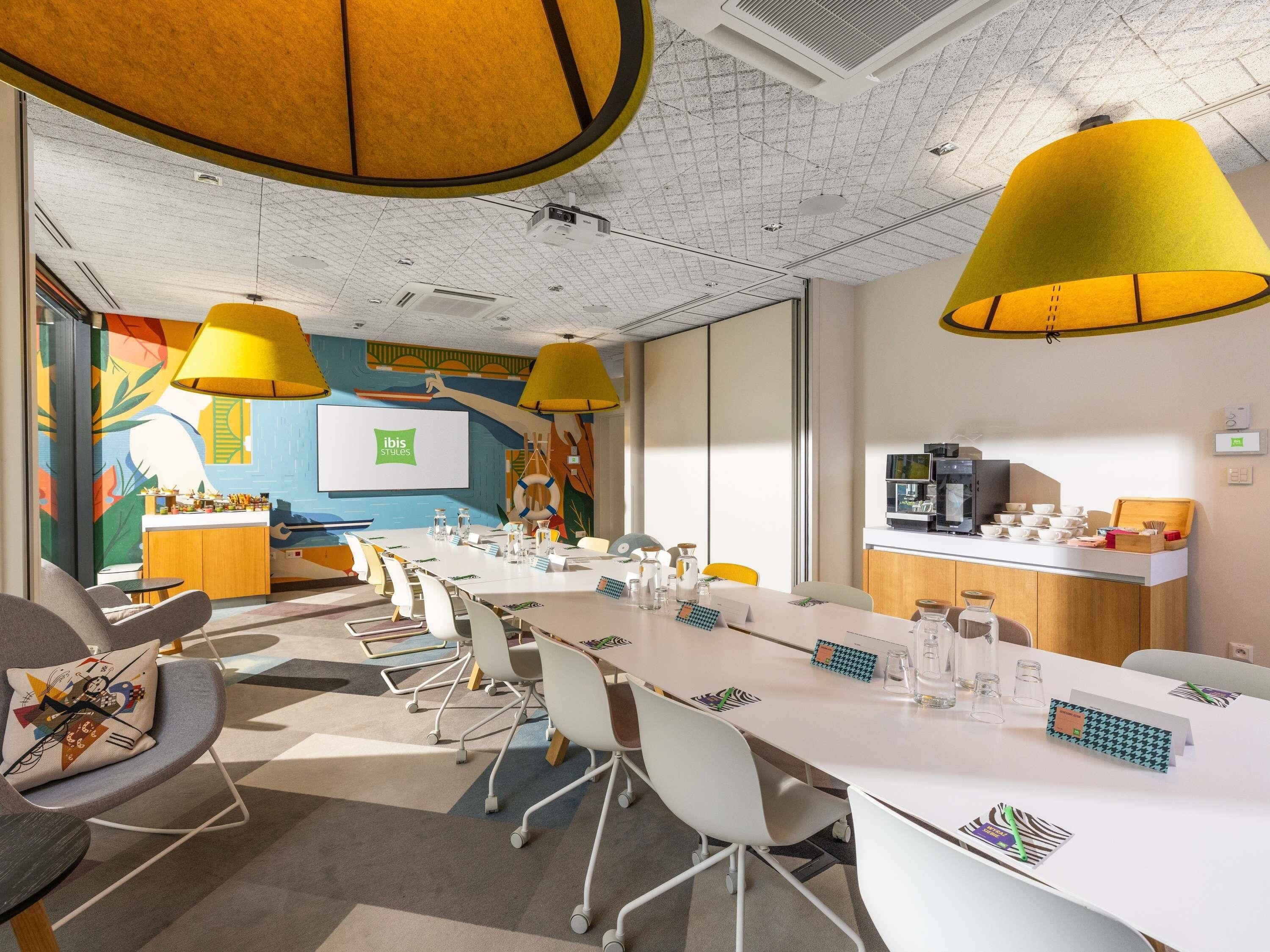 A modern conference room with a long table, chairs, a projector screen, and a coffee station.