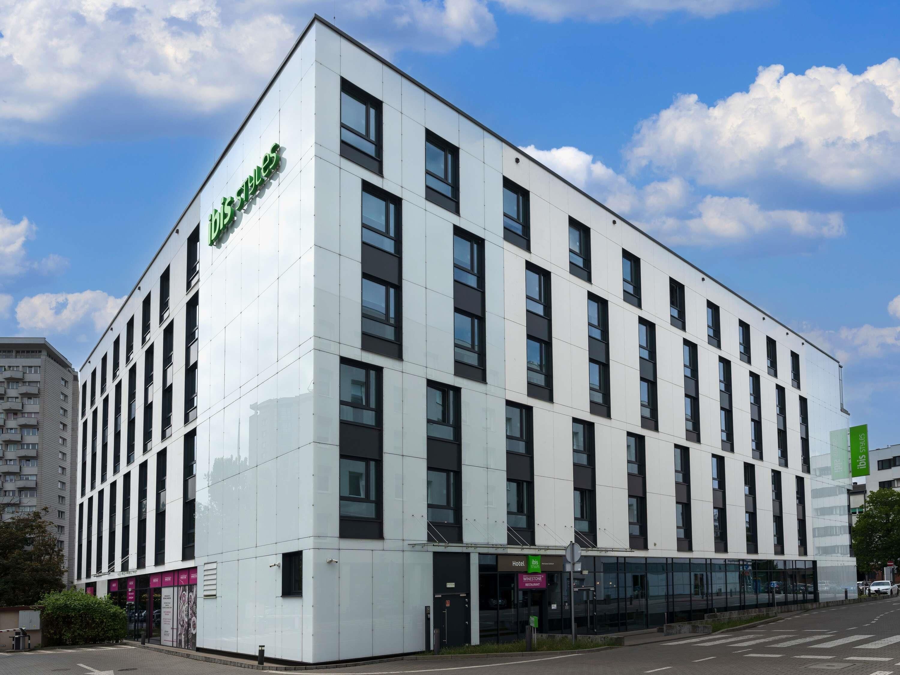 Un moderno edificio de hotel con un llamativo logotipo verde, múltiples ventanas y un cielo despejado.