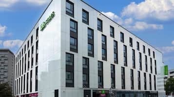 Un moderno edificio de hotel con un llamativo logotipo verde, múltiples ventanas y un cielo despejado.