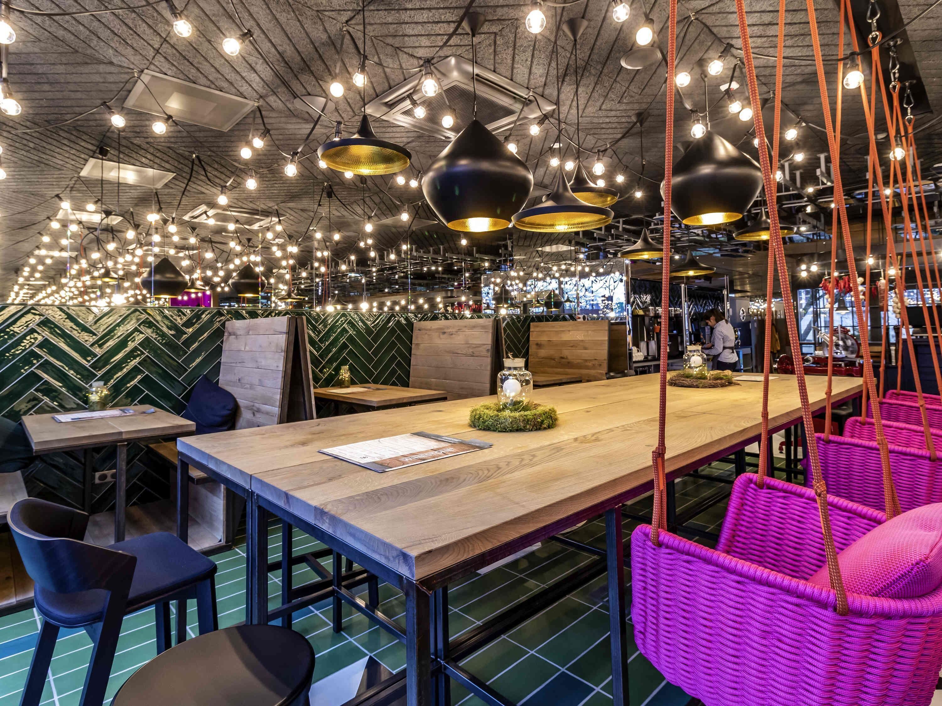 A restaurant interior with hanging pendant lights, a long wooden table, and seating areas.