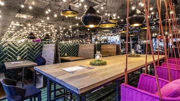 A restaurant interior with hanging pendant lights, a long wooden table, and seating areas.